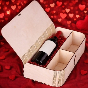 May include: A wooden wine box with a bottle of red wine inside. The box is divided into three compartments and lined with red paper. The box is open, revealing the wine bottle with a blank label. The background is a red fabric with heart shapes.