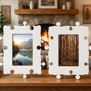 May include: Two white puzzle-shaped picture frames with landscape photos. The frames are made of a light-colored material and have a unique jigsaw puzzle design. One frame displays a mountain lake scene, and the other shows a forest.