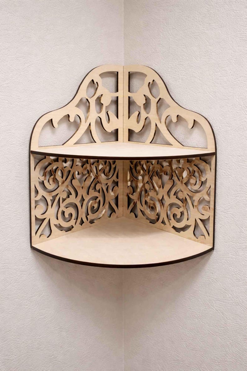 May include: A wooden corner shelf with an ornate, openwork design. The shelf has two tiers and a decorative top with a curved shape. The edges are dark brown, and the shelf is made of light-colored wood.