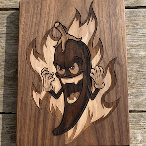 Può includere: Targa in legno raffigurante un peperoncino dei cartoni animati con un'espressione arrabbiata, su uno sfondo di fiamme. Il peperoncino è marrone con guanti color beige e un ampio sorriso. Le fiamme sono di una tonalità di marrone più chiara.