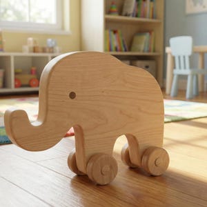May include: A light brown wooden elephant toy with a trunk and ears, mounted on four wooden wheels. The toy is designed for young children. It is sitting on a wooden floor in a room with a window and bookshelves.