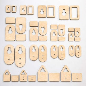 Op de afbeelding: Een verzameling van diverse houten sleutelgat hangers en montage hardware. De stukken zijn van onafgewerkt, lichtgekleurd hout en omvatten rechthoekige, ovale en driehoekige vormen met sleutelgatsleuven en montagegaten. De hardware is gerangschikt op een wit oppervlak.