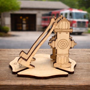 May include: A wooden fire hydrant and axe-shaped phone stand. The stand is light brown with dark brown accents. The base is shaped like a Maltese cross with the number 12 and the word "ND" visible. A fire truck is in the background.
