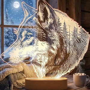 May include: A decorative wolf-shaped night light with a detailed etched design. The light is set on a wooden base and emits a warm glow. The wolf's profile is visible, with a forest scene etched into the design. A cozy winter scene is visible in the background.