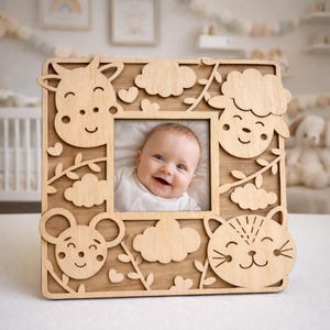 May include: Wooden baby photo frame with a smiling baby in the center. The frame is decorated with laser-cut animal shapes, including a cow, sheep, mouse, and cat, along with clouds and vines. The frame is made of light-colored wood.