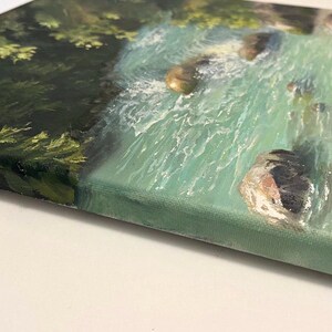May include: A canvas painting of a turquoise river scene with rocks and green foliage. The artwork is viewed from a side angle, revealing the textured brushstrokes and the canvas edge. The painting uses metric measurements.