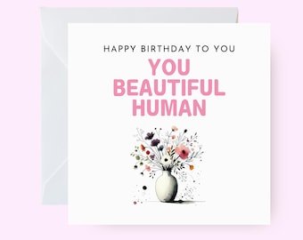 Puede incluir: Feliz cumpleaños, hermoso humano. Una tarjeta blanca con texto rosa y una ilustración de acuarela de un ramo de flores en un jarrón blanco.