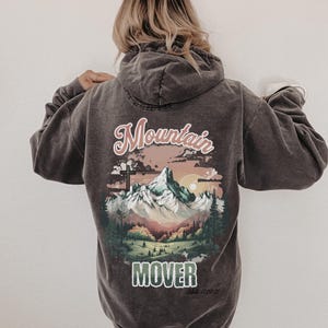 Peut inclure: Un sweat à capuche gris foncé avec une scène de montagne et le texte "Mountain Mover" et "Matt. 17:20-21".