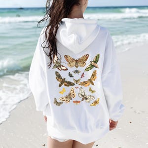 May include: White hoodie with a graphic print of various butterflies in shades of brown, green, and yellow on the back.