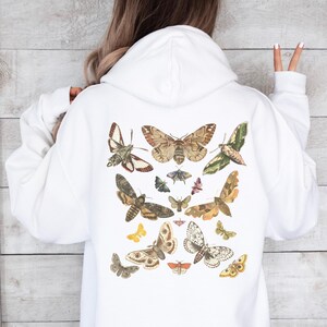 May include: White hoodie with a vintage illustration of various butterflies and moths printed on the back. The butterflies and moths are in shades of brown, white, black, and yellow.