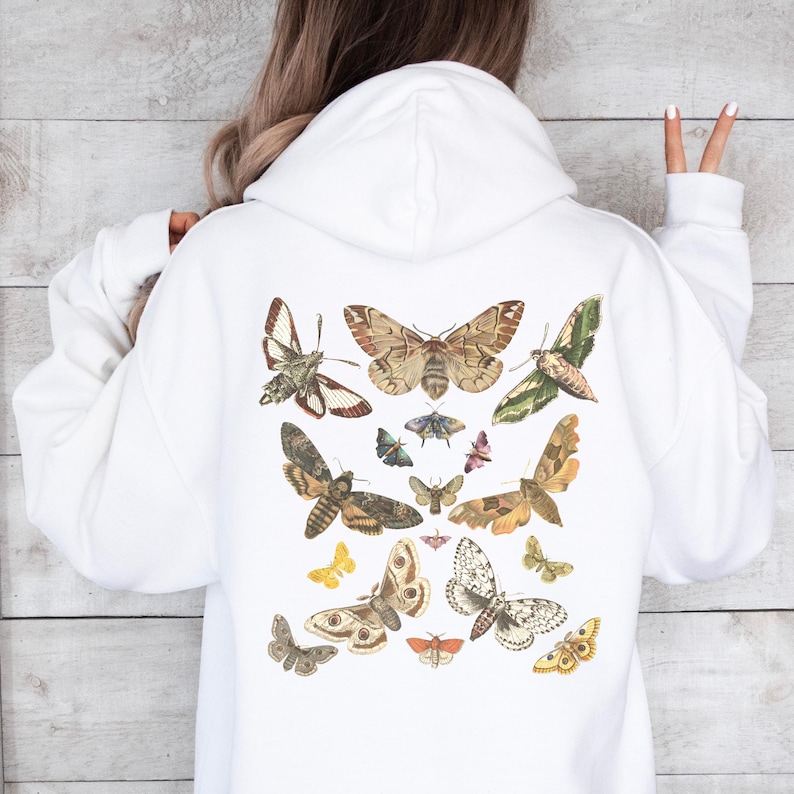 May include: White hoodie with a vintage illustration of various butterflies and moths printed on the back. The butterflies and moths are in shades of brown, white, black, and yellow.