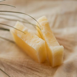 May include: Close-up of three pieces of pale yellow cheese stacked on top of each other. The cheese is on a light brown surface.