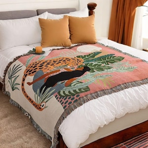 May include: A pink and white woven throw blanket with a fringed edge features a colourful illustration of a leopard and a black panther in a jungle setting.
