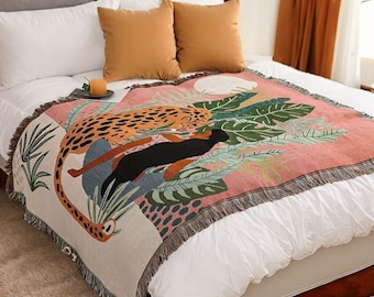 May include: A pink and white woven throw blanket with a fringed edge features a colorful illustration of a leopard and a black panther in a jungle setting.