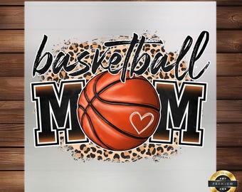 Puede incluir: Un fondo blanco con un diseño de baloncesto marrón y negro. El baloncesto tiene un corazón en él. El texto "basketball mom" está en negro con contornos marrones. El fondo tiene un patrón de estampado de leopardo.