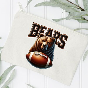 May include: A white canvas makeup bag with a brown bear holding a football. The text "BEARS" is printed in black letters.