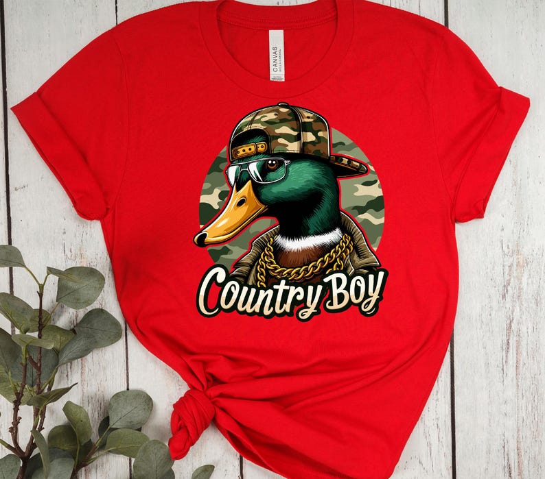May include: Red t-shirt featuring a graphic of a duck wearing a camouflage hat, sunglasses, and a gold chain. The text "Country Boy" is printed below the duck.