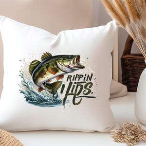 Może przedstawiać: Biała poduszka z grafiką przedstawiającą okonia dużego wyskakującego z wody z napisem "Rippin Lips" czarnymi literami.