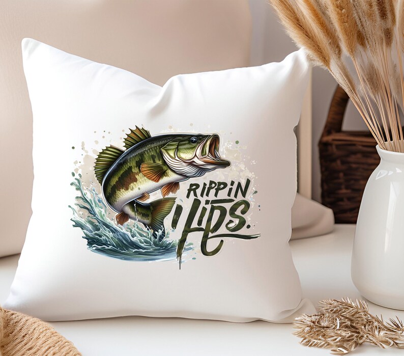 Może przedstawiać: Biała poduszka z grafiką przedstawiającą okonia dużego wyskakującego z wody z napisem "Rippin Lips" czarnymi literami.