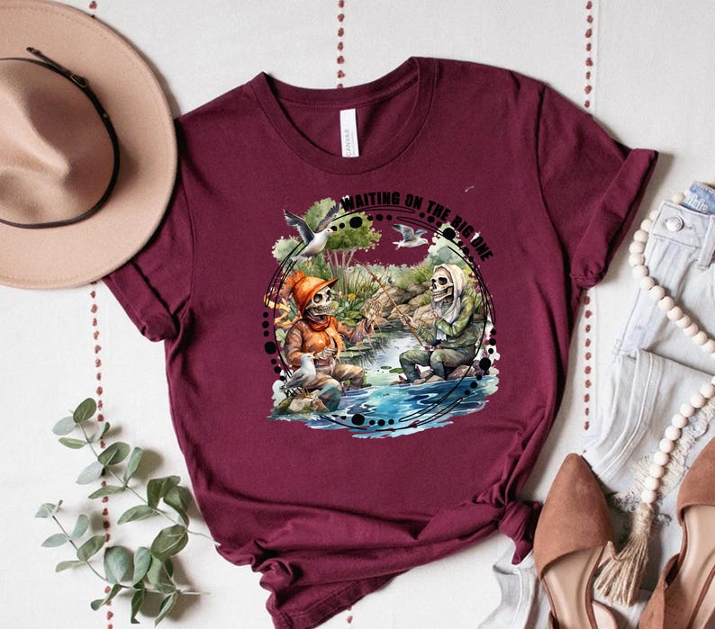 K&ouml;nnte beinhalten: Ein maroonfarbenes T-Shirt mit einem Motiv von zwei Skeletten beim Angeln mit dem Text "Waiting on the big one".
