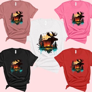 May include: Five different color t-shirts featuring a moose silhouette with a sunset and trees in the background. The t-shirts are available in pink, red, black, white, and dusty rose.