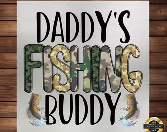 May include: A white background with the text "Daddy's Fishing Buddy" in black. The word "Fishing" is in a camouflage pattern. There are two cartoon fish on either side of the text.