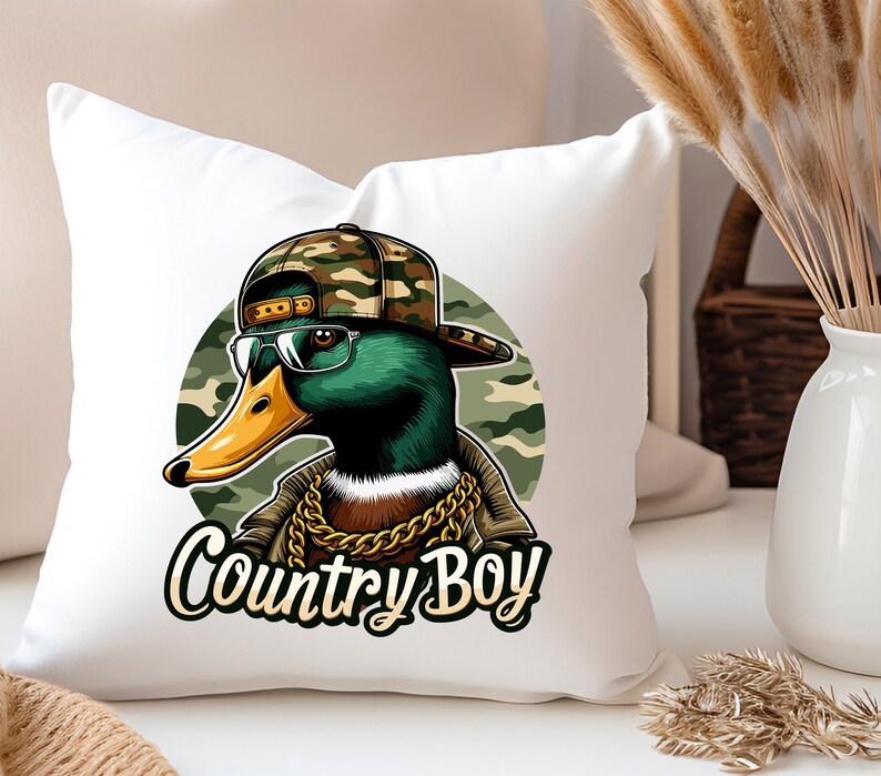May include: A white cushion featuring a green duck wearing a camouflage hat and sunglasses. The duck is sporting a gold chain and the text "Country Boy" is printed beneath the duck.