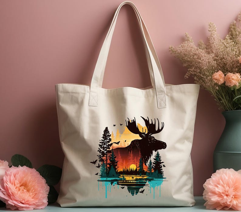 May include: A white canvas tote bag with a silhouette of a moose standing in front of a sunset landscape. The moose is black and the landscape is a gradient of orange, yellow, and blue. The bag has two black handles.
