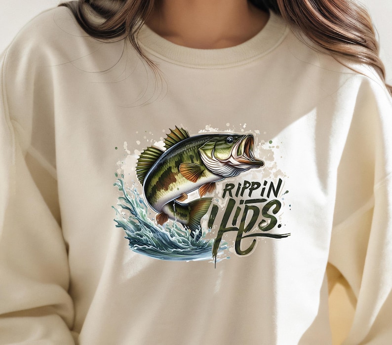 Może przedstawiać: Kremowa bluza z nadrukiem dużego okonia, kt&oacute;ry wyskakuje z wody. Nadruk zawiera tekst "Rippin' Lips".