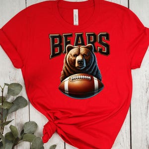 May include: Red t-shirt with a brown bear holding a football and the word "BEARS" in black letters.