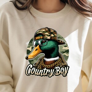May include: A white sweatshirt featuring a graphic of a duck wearing a camouflage baseball cap, sunglasses, and a gold chain. The text "Country Boy" is printed below the duck.