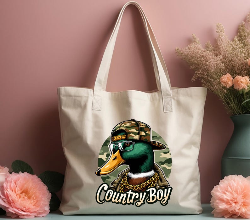 May include: A white canvas tote bag featuring a cartoon duck wearing a camouflage hat and sunglasses. The duck is sporting a gold chain and the text "Country Boy" is printed beneath it.