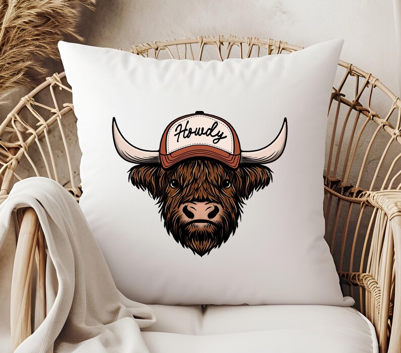 May include: White throw pillow featuring a cartoon illustration of a Highland cow wearing a brown and white baseball cap. The cap has the word "Howdy" in black script. The cow has long brown fur and large horns.