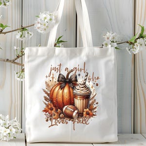 May include: White tote bag with a brown pumpkin, a cup of coffee, and a football. The text on the bag reads "Just a girl who loves fall".