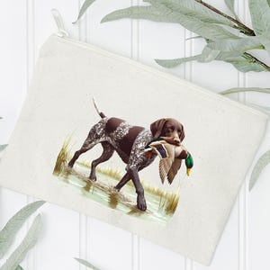 Puede incluir: Una bolsa de lona blanca con cremallera que muestra un perro Braco Alem&aacute;n de Pelo Corto marr&oacute;n y blanco llevando un pato silvestre verde y marr&oacute;n en la boca. El perro est&aacute; de pie en una zona herbosa con agua.