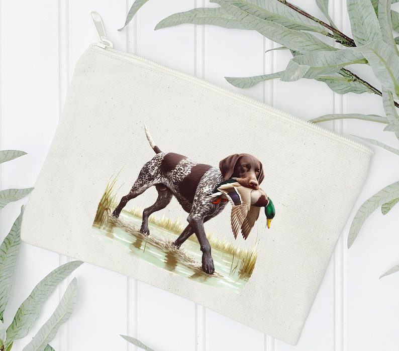 Puede incluir: Una bolsa de lona blanca con cremallera que muestra un perro Braco Alem&aacute;n de Pelo Corto marr&oacute;n y blanco llevando un pato silvestre verde y marr&oacute;n en la boca. El perro est&aacute; de pie en una zona herbosa con agua.