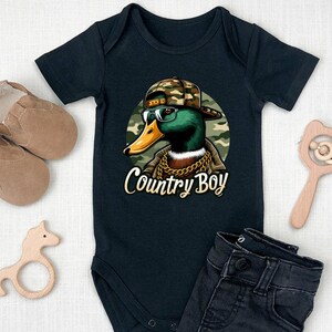 May include: Black baby bodysuit featuring a cartoon illustration of a duck wearing a camouflage hat, sunglasses, and a gold chain. The text "Country Boy" is printed below the duck.