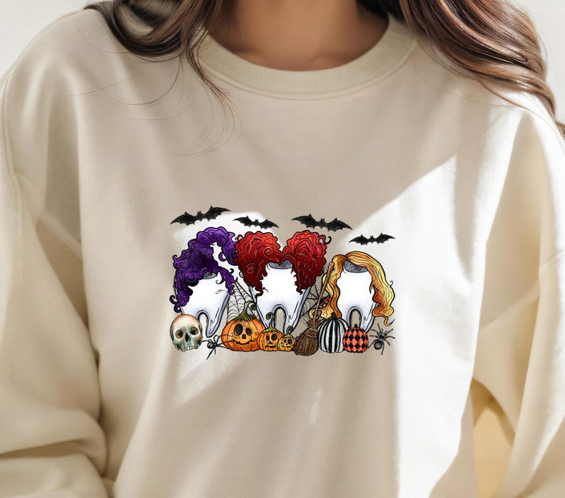 May include: A white sweatshirt with a Halloween-themed graphic featuring three cartoon teeth dressed as witches with pumpkins and bats. The text "Boo-tiful" is printed on the sweatshirt.