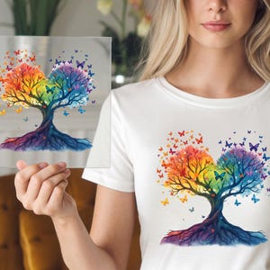 May include: A white t-shirt with a colorful watercolor design of a tree with butterflies. The tree is made up of two trees that are intertwined and have roots that are connected. The butterflies are flying around the tree and are in various colors.