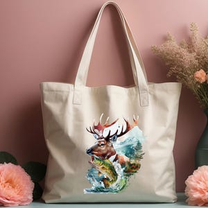 May include: A beige canvas tote bag with a watercolour illustration of a deer with large antlers, a fish, and a mountain scene. The bag has two handles and is suitable for carrying various items.