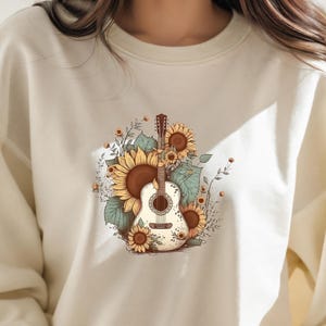May include: A cream-colored sweatshirt with a graphic print of a guitar surrounded by sunflowers. The guitar is white with brown accents and the sunflowers are yellow with brown centers.