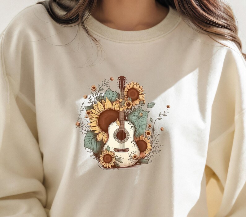 May include: A cream-colored sweatshirt with a graphic print of a guitar surrounded by sunflowers. The guitar is white with brown accents and the sunflowers are yellow with brown centers.