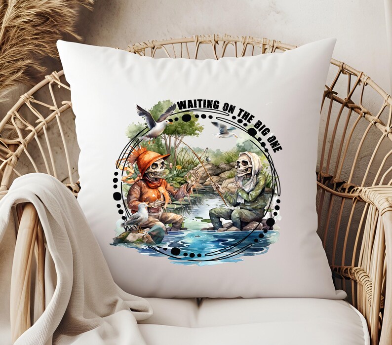 K&ouml;nnte beinhalten: Ein wei&szlig;es Kissen mit einer Aquarell-Illustration von zwei Skeletten, die in einem See angeln. Der Text "Waiting on the Big One" ist in einem Kreis um die Skelette geschrieben.