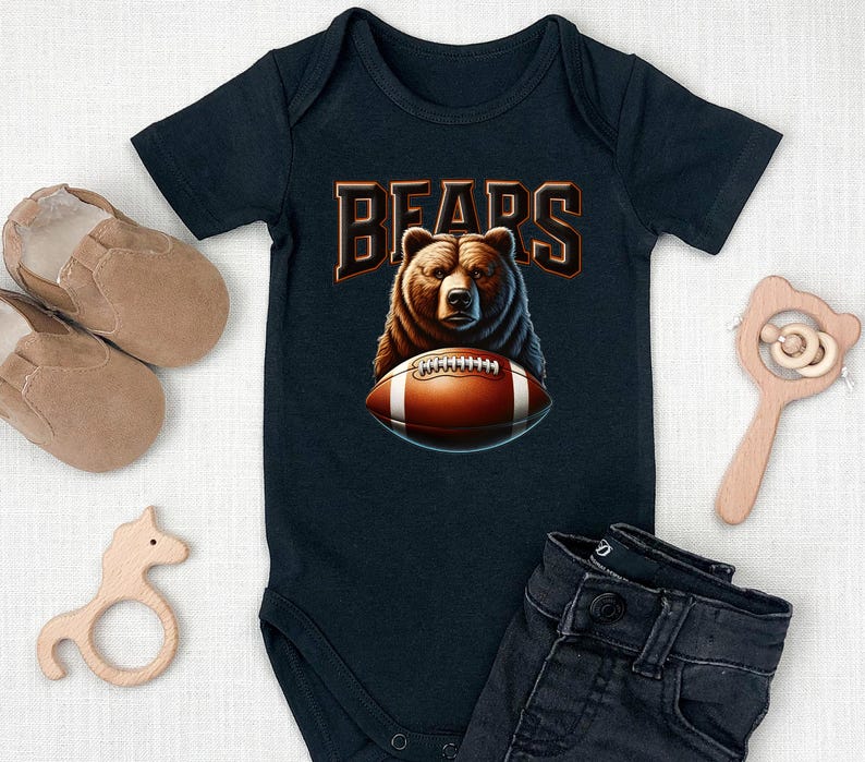 May include: A black baby onesie with a brown bear wearing a football helmet and holding a football. The onesie has the word "BEARS" printed on it in orange letters.