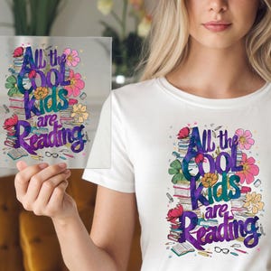 May include: White t-shirt with a colorful graphic design featuring a stack of books, flowers, and the text "All the Cool Kids are Reading".