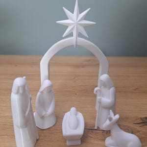 Peut inclure: Une crèche blanche comprenant une étoile, une arche et des figurines de Marie, Joseph, l'enfant Jésus et un âne. Les figurines sont stylisées et minimalistes, parfaites pour la décoration de Noël.