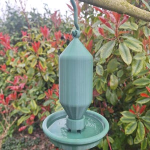 May include: A sage green bird feeder featuring a cylindrical reservoir with a tapered top and a circular feeding tray at the base. The feeder is suspended by a matching green hook. The text DOWNLOAD FILE is printed in white on a red background.