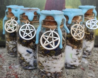 Puede incluir: Cinco pequeñas botellas de vidrio con cera azul goteando por los lados. Cada botella contiene una mezcla de hierbas y cristales y tiene un amuleto de pentagrama plateado colgando del tapón de corcho.