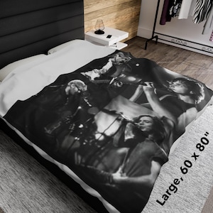 Puede incluir: Manta en blanco y negro con una banda actuando en el escenario. La manta es grande, mide 152 x 203 cm. La imagen muestra a músicos tocando instrumentos y cantando en micrófonos. La manta está sobre una cama.