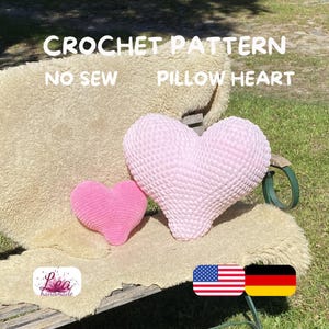 Könnte beinhalten: Zwei herzförmige Häkelkissen in Hellrosa und Pink. Das größere Kissen ist strukturiert und das kleinere glatt. Der Text "CROCHET PATTERN NO SEW PILLOW HEART" befindet sich oben im Bild. Das Bild enthält auch die amerikanische und deutsche Flagge.